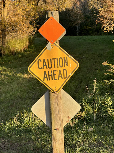 a caution sign on a wooden post in the grass