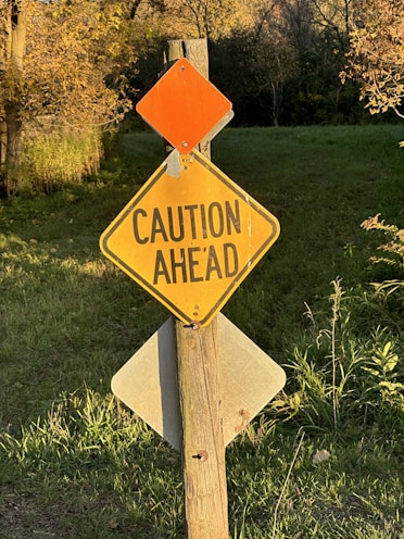 a caution sign on a wooden post in the grass
