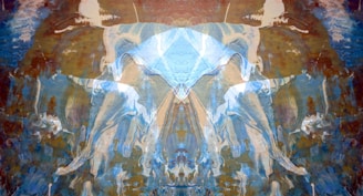 An abstract composition featuring symmetrical patterns resembling a Rorschach test. The image is dominated by hues of blue and brown, with fluid, wave-like shapes. The patterns evoke a sense of movement and depth, possibly resembling ethereal figures or forms.