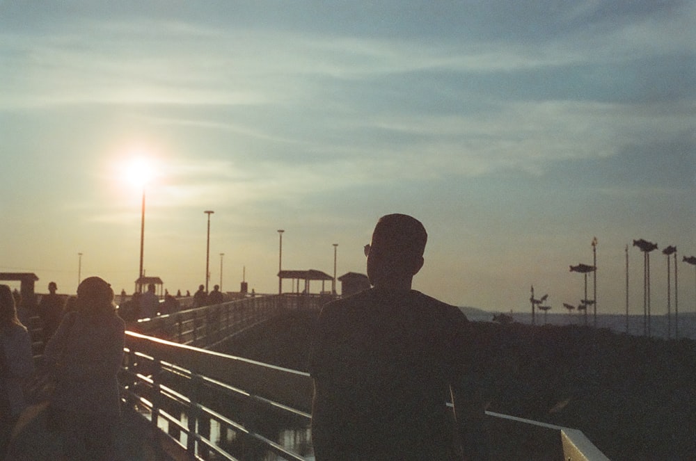 um homem está de pé em um píer vendo o sol se pôr