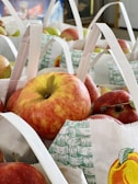 Bags filled with red and green apples are neatly arranged, with the fruits peeking out and each bag having a decorative design featuring fruit illustrations.