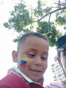 A smiling child with a vibrant butterfly face paint design at a sunny outdoor party.