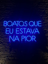 A neon sign displaying a phrase in Portuguese, illuminated in bright blue against a dark brick wall.