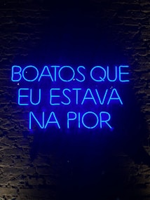 A neon sign displaying a phrase in Portuguese, illuminated in bright blue against a dark brick wall.