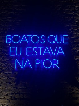 A neon sign displaying a phrase in Portuguese, illuminated in bright blue against a dark brick wall.