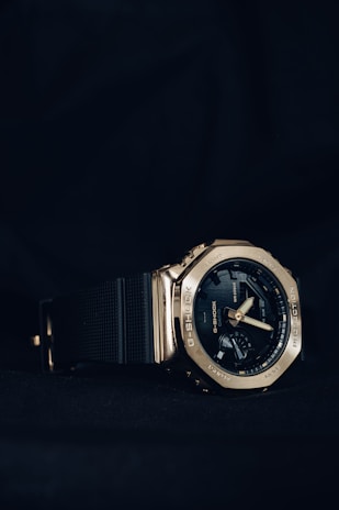 A stylish analog-digital wristwatch with a metallic bezel and black rubber strap. The watch face displays multiple dials and features, including the brand name. The lighting highlights the watch's polished metallic finish against a dark background.
