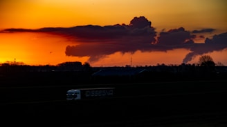 A red delivery truck speeding down a highway at sunset.