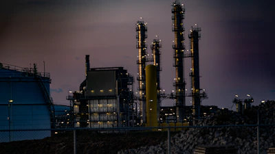 A powerful industrial fire suppression system activating within a sprawling refinery at dusk.