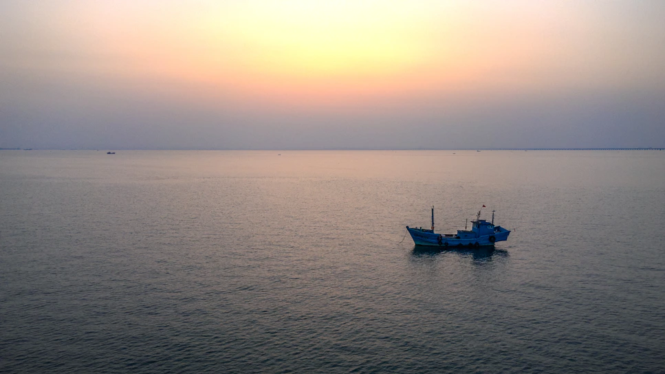 Sunset over a calm lake with a lone fishing boat drifting peacefully