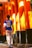 A person wearing a sports jersey with the name and number 'Neymar Jr 10' walks through a passageway lined with tall, vibrant orange pillars. The pillars are partially shaded and have some text written on them, likely in Japanese characters. The ground is paved, and the scene is illuminated by warm sunlight.