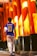 A person wearing a sports jersey with the name and number 'Neymar Jr 10' walks through a passageway lined with tall, vibrant orange pillars. The pillars are partially shaded and have some text written on them, likely in Japanese characters. The ground is paved, and the scene is illuminated by warm sunlight.