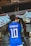 A person is wearing a blue soccer jersey with 'Neymar Jr' and the number '10' on the back, standing in front of a traditional shrine. The shrine features stone statues and rope decorations, with a white cloth adorned with red symbols.