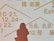 Silhouette of a person standing in front of a light background displaying text in multiple languages, including dates and terms related to exhibitions. The text is written in bold, prominent letters in orange color.