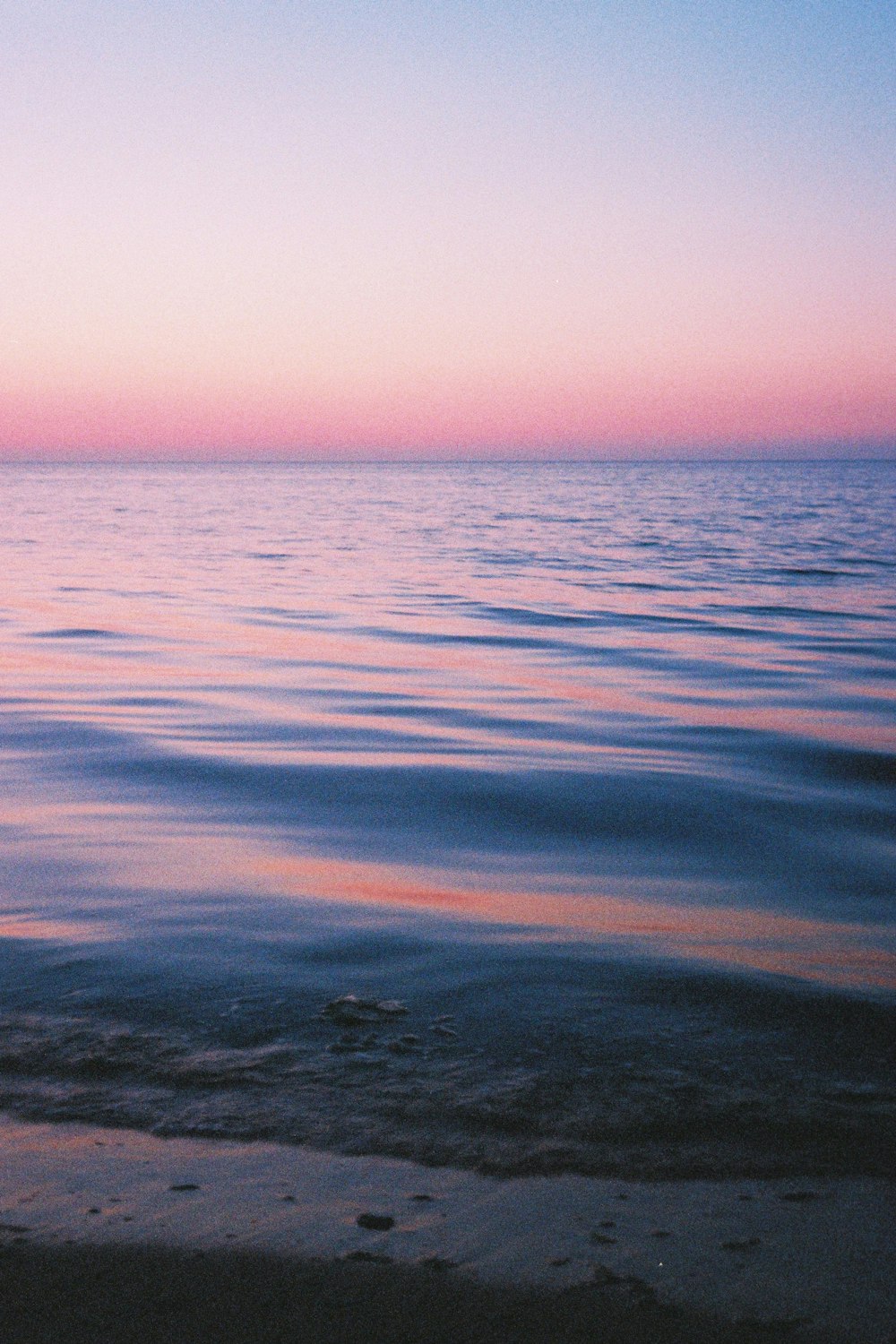 a body of water with a pink sky in the background