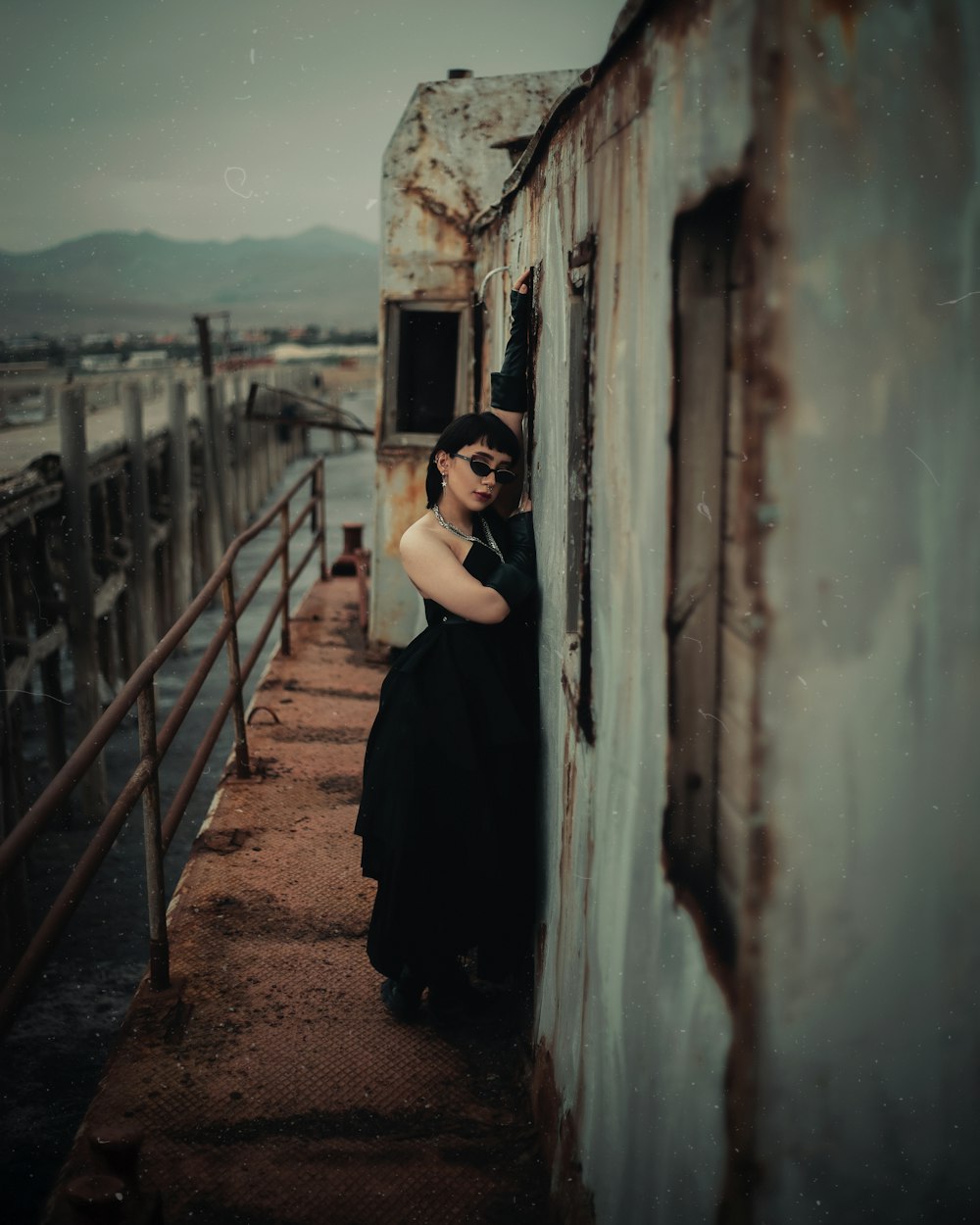 a woman in a black dress leaning against a wall