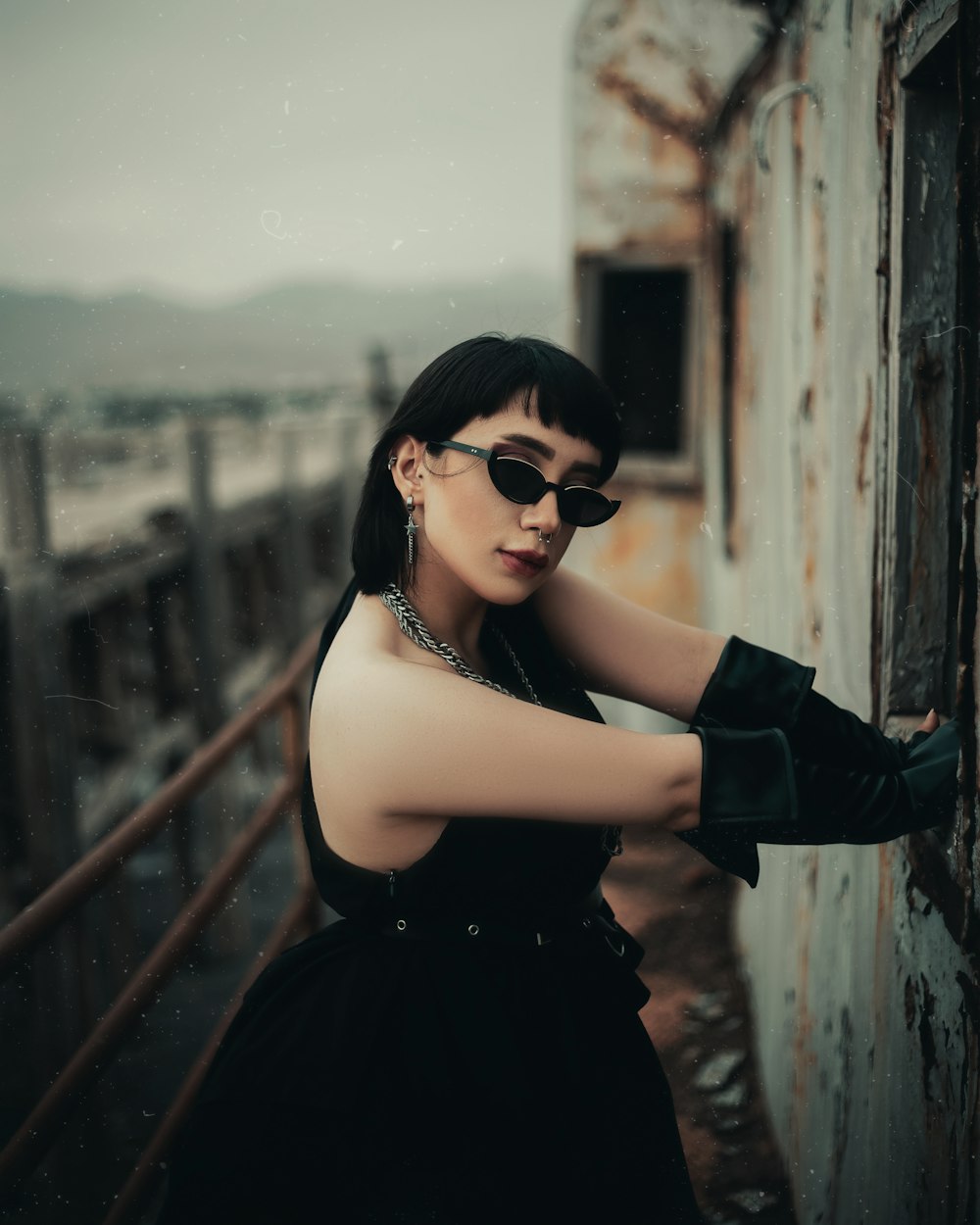 a woman in a black dress and sunglasses leaning against a wall