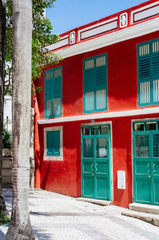 Before and after transformation of a traditional Alicante building facade painted with vibrant carmesí rojo and complemented by forest green accents.