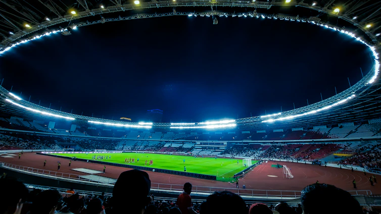 A vibrant soccer stadium under bright lights with players in action and fans cheering.