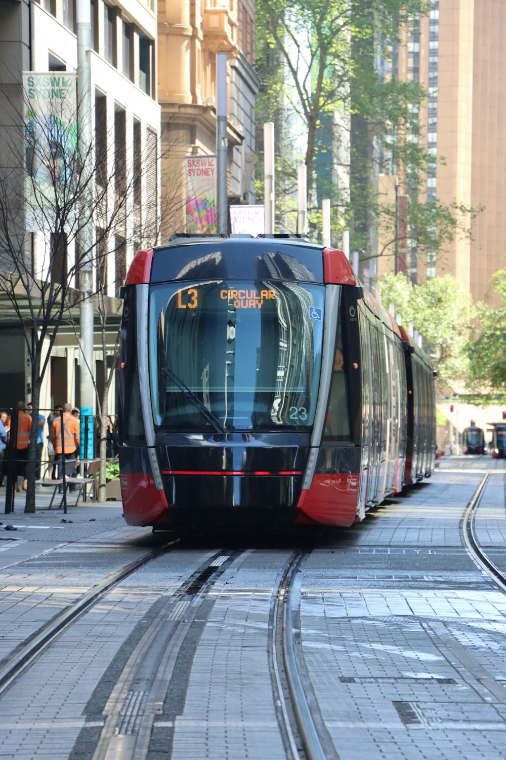 a red and black train traveling down a street next to tall buildings