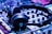 A pair of black headphones is placed on a DJ mixer. The mixer has various knobs and sliders, and the lighting gives off a blue-tinted ambiance, suggesting a musical or party setting.