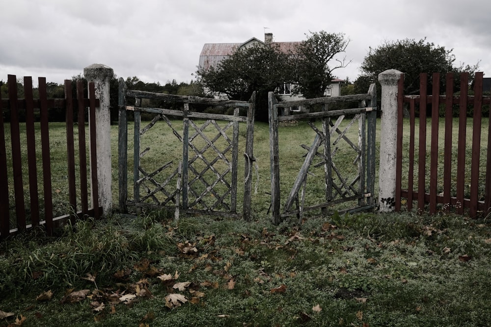 a wooden gate in a grassy field with a house in the background