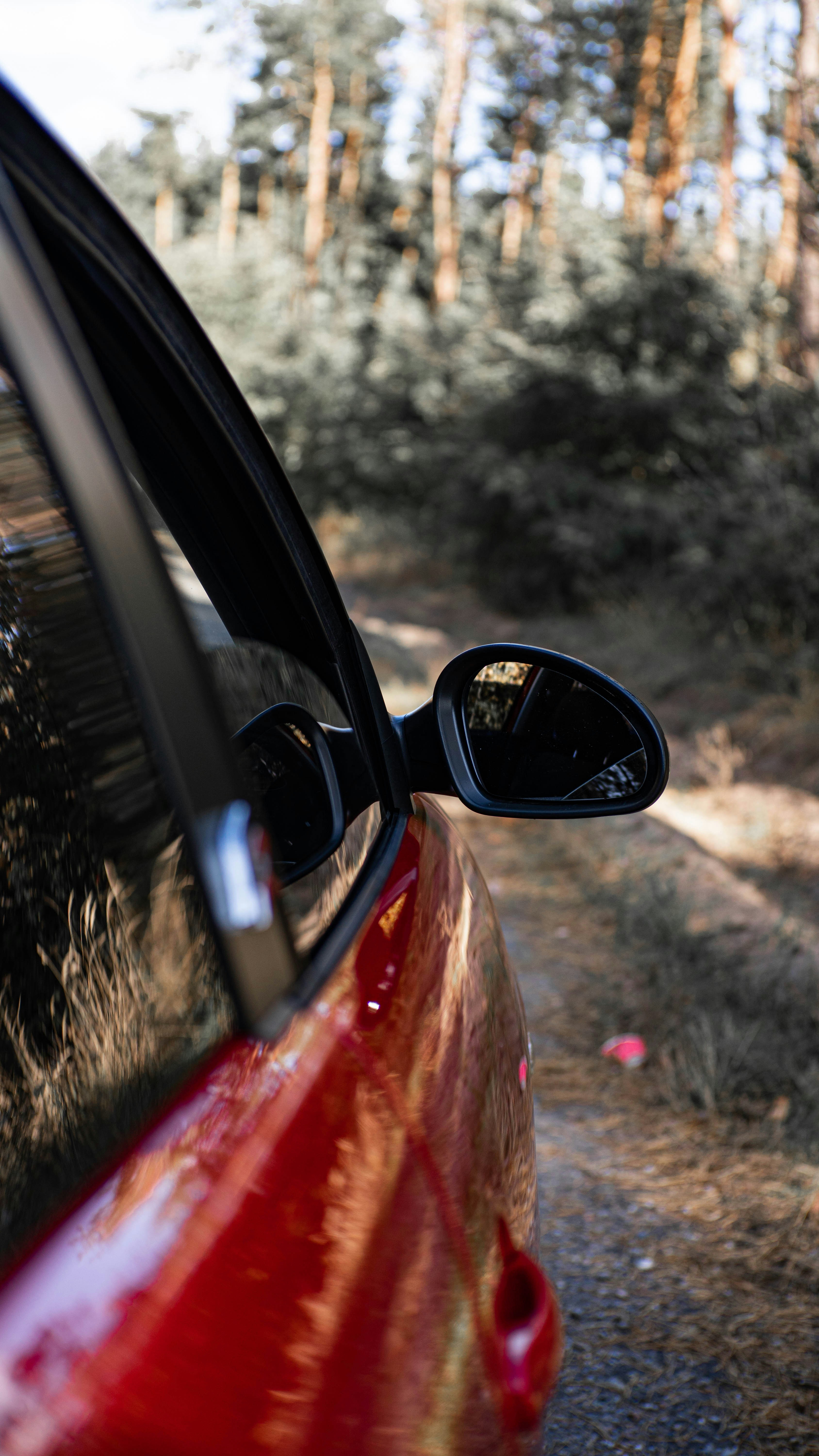 a red car parked on a dirt road next to a forest