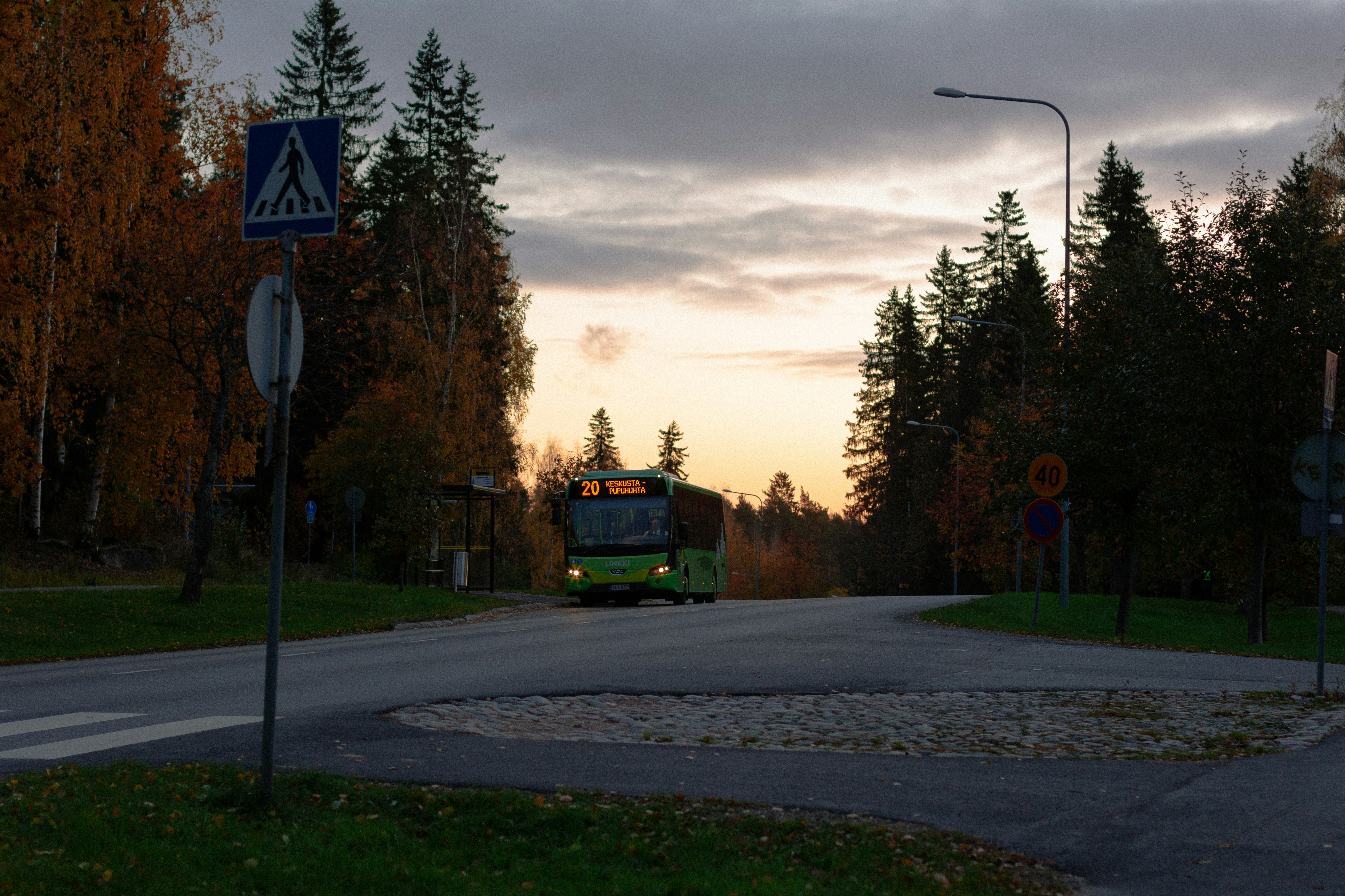 a green bus driving down a street next to a forest