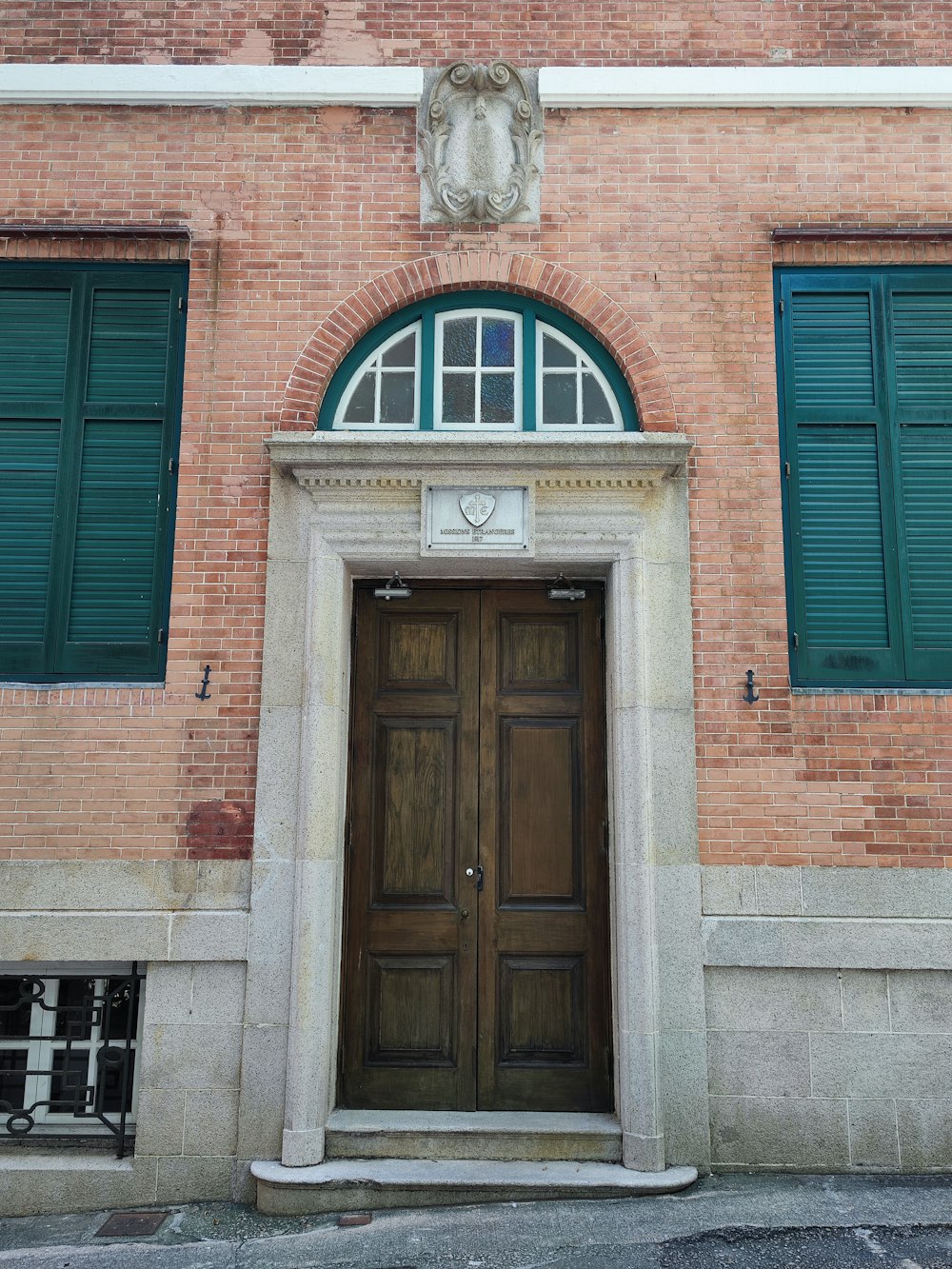 a brick building with green shutters and a wooden door
