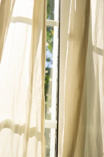 Soft cream curtains framing a window with a view of a quiet garden.