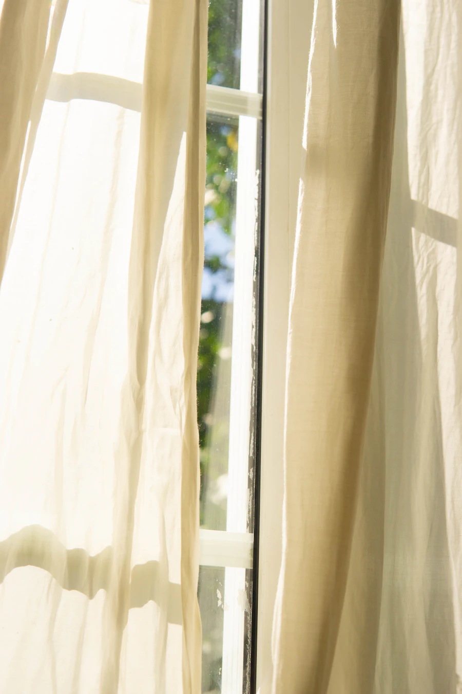Cortinas franzidas em tecido claro junto a uma janela iluminada