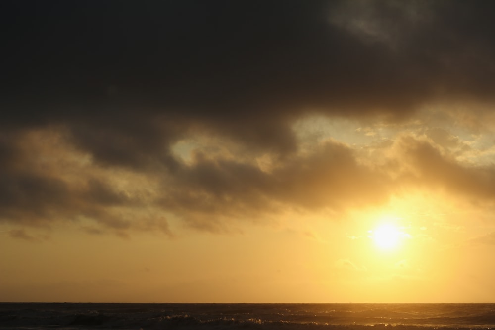 the sun is setting over the ocean on a cloudy day