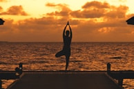 Guests practicing yoga on a wooden deck overlooking a calm ocean at sunset.