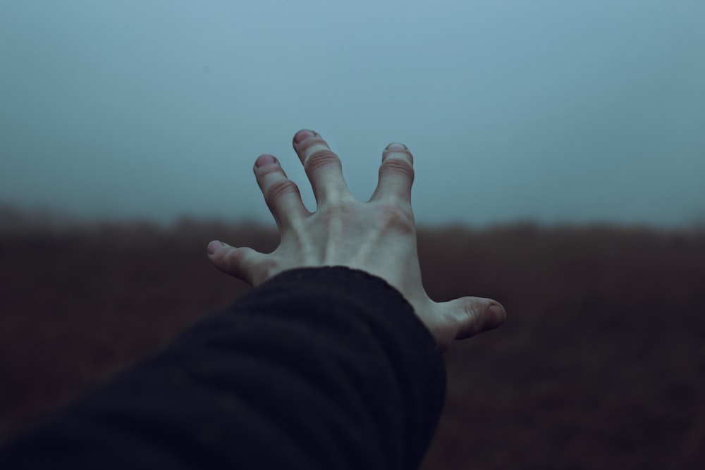 a person's hand reaching out towards the sky