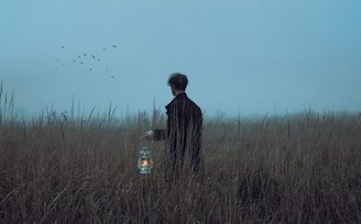 a man standing in a field holding a lantern