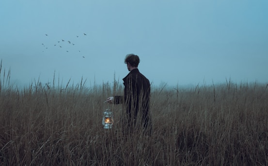 a man standing in a field holding a lantern