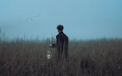 a man standing in a field holding a lantern