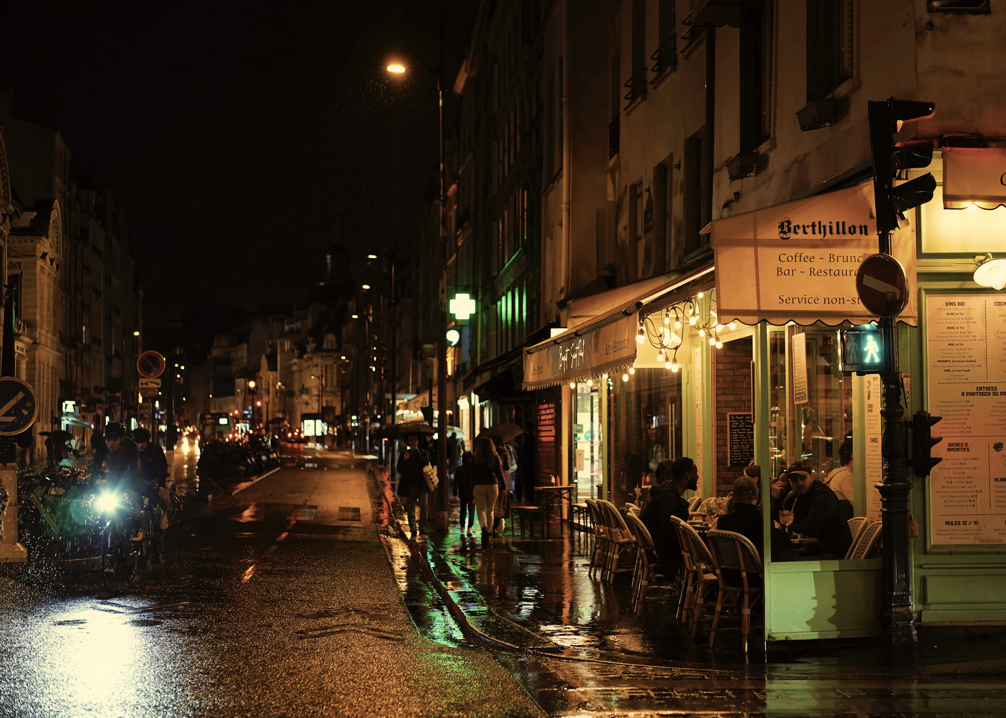 A city street at night with people sitting at tables