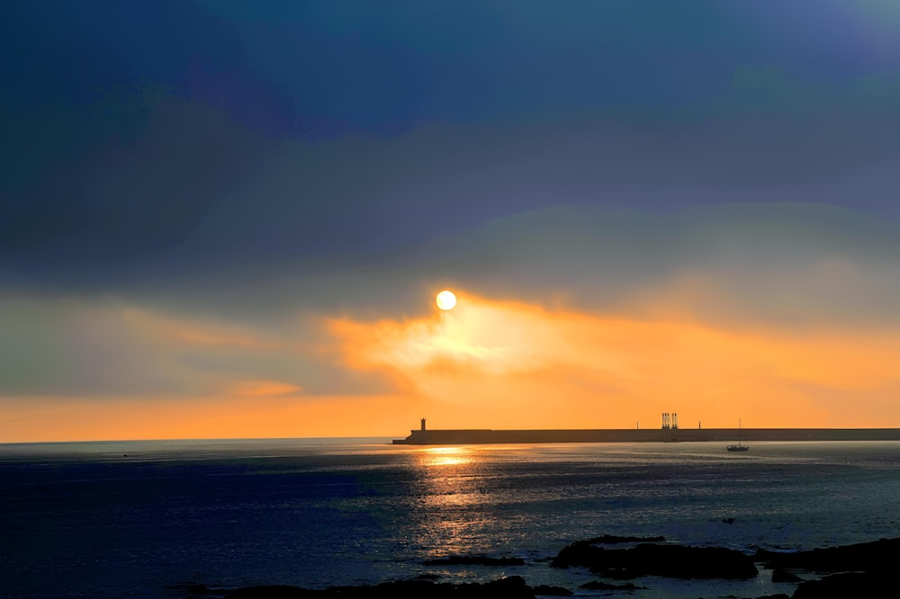 the sun is setting over the ocean with a lighthouse in the distance