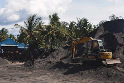 A bright yellow excavator working on a construction site surrounded by tropical greenery.