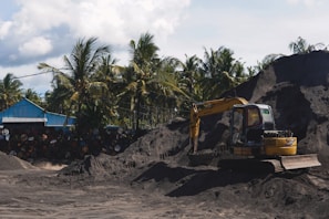 An excavator lifting earth near a vibrant orange grove under a bright blue sky.