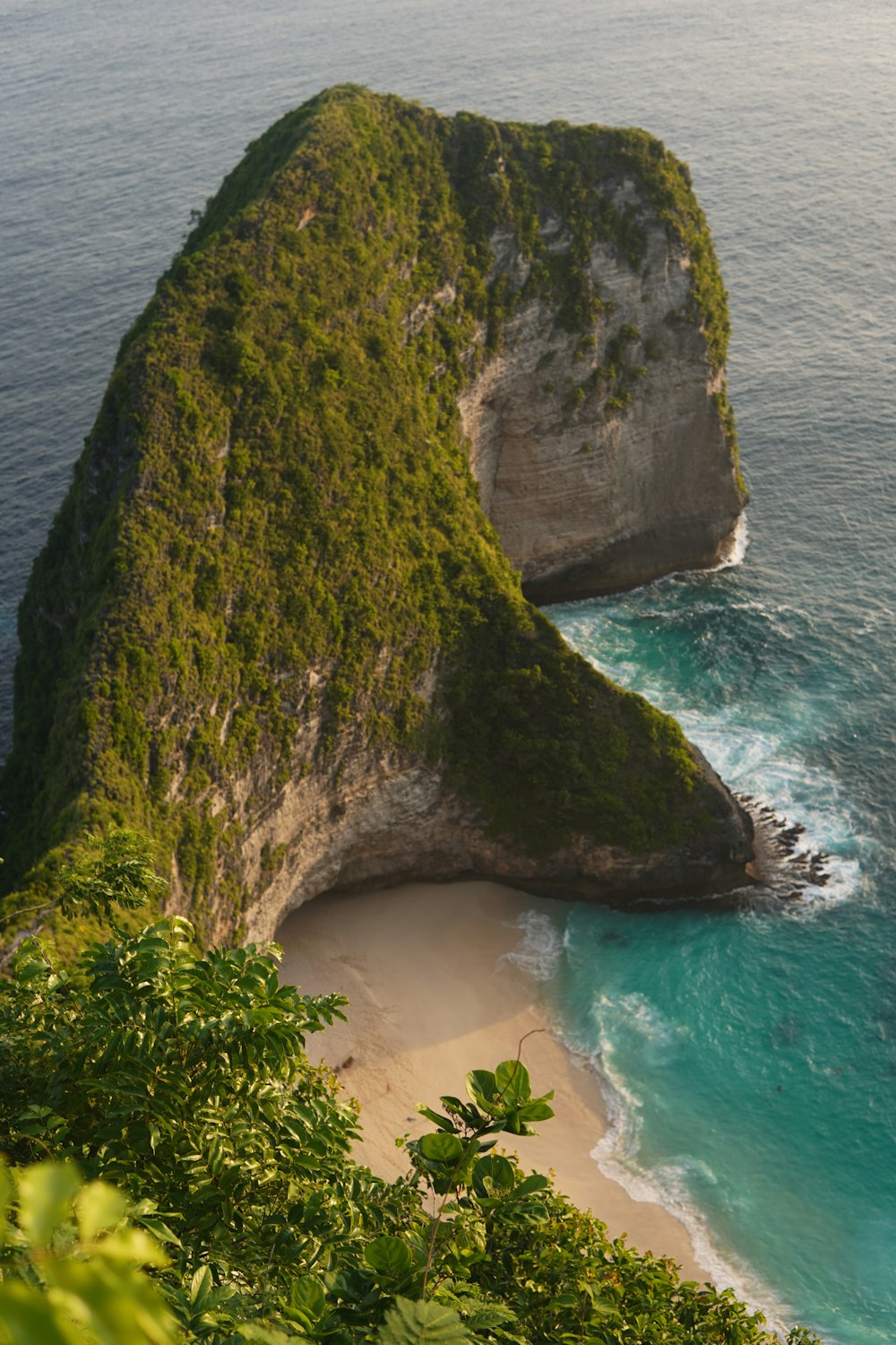 a large rock sticking out of the ocean next to a beach