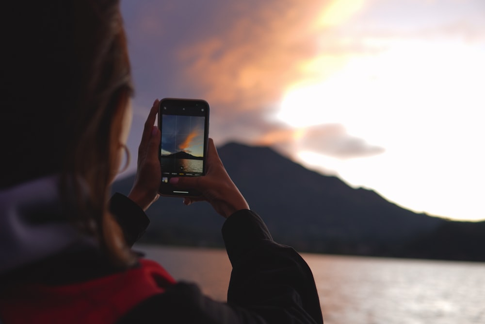 a woman taking a picture of a sunset with her cell phone