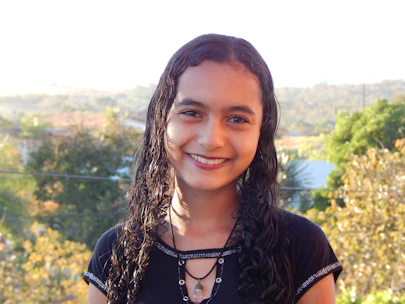Close-up of a woman with beautifully textured curly hair smiling outdoors in natural light.