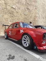 A sleek red sports car with a custom racing livery featuring bold stripes and sponsor logos.