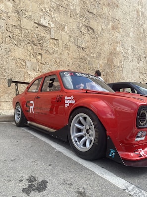 A sleek red sports car with a custom racing livery featuring bold stripes and sponsor logos.