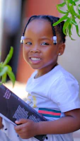 A close-up of a child’s joyful face holding a book donated by Highly Favored Foundation during a literacy outreach.