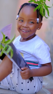 a little girl sitting on the ground with a plant in her hand