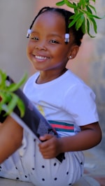 a young girl sitting on the ground with a plant in her hand