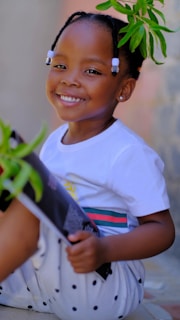 a young girl sitting on the ground with a plant in her hand