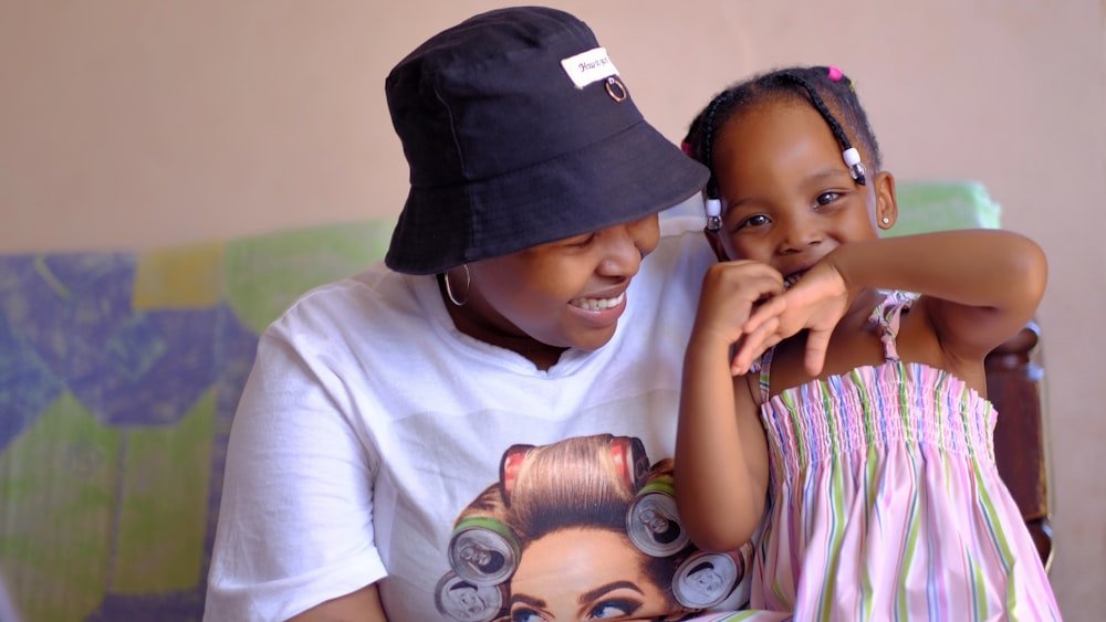 a woman sitting next to a little girl wearing a hat